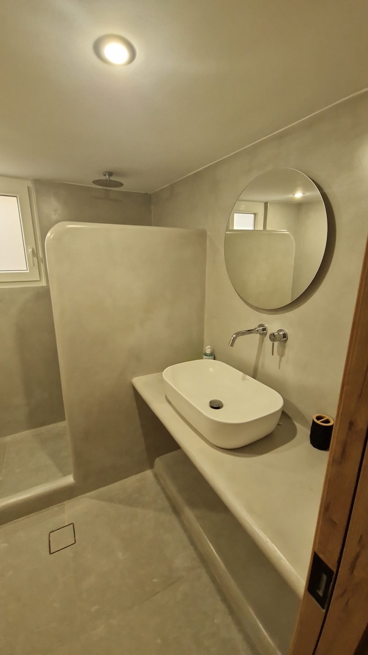 Actual Alya Paros bathroom with a sculpted basin, circular mirror and walk-in shower